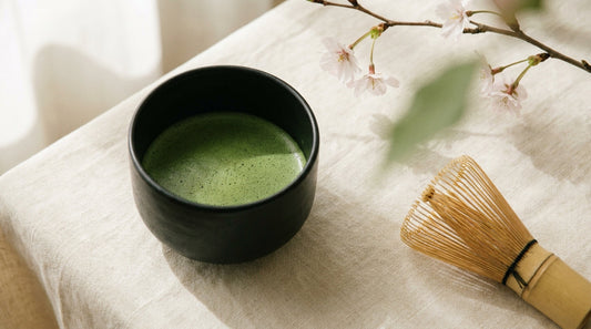 Chawan de cerámica negra con matcha jade recién batido, chasen de bambú y rama de cerezo — ritual matcha Tea Forté
